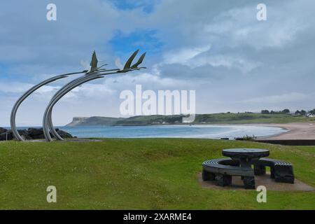 Enfants de LIR Cygnes sculpture, un banc en pierre circulaire sur le front de mer de Ballycastle, Irlande du Nord, avec une mer bleue, ciel bleu et fond de montagnes Banque D'Images