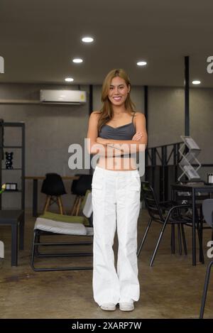 Portrait en longueur de belle jeune asiatique debout à l'intérieur et portant des vêtements professionnels avec les bras croisés regardant la caméra Banque D'Images