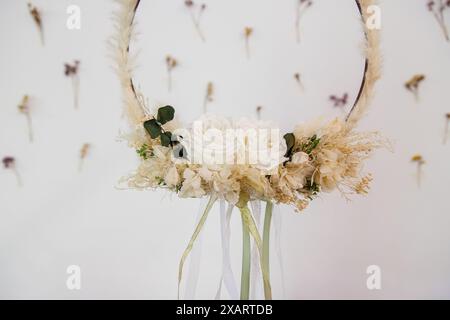 Élégant cerceau floral orné de roses blanches préservées et de fleurs séchées, suspendu sur fond de fleurs séchées scotchées. Banque D'Images