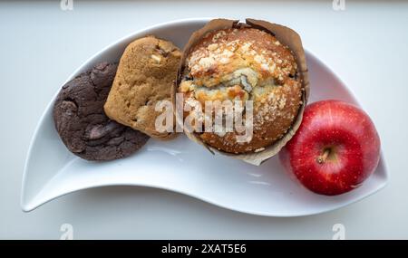 Un assortiment vibrant de friandises, avec une pomme rouge croustillante, habilement agencée sur une assiette blanche incurvée. Banque D'Images