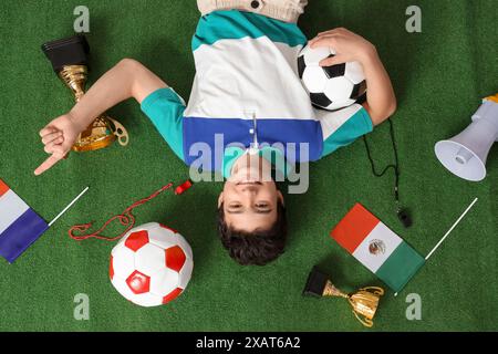 Adolescent avec des ballons de football, des drapeaux et des tasses d'or couché sur l'herbe verte Banque D'Images