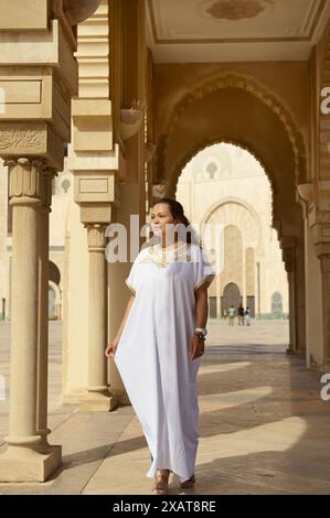 Portrait pleine longueur de jolie femme multi ethnique en robe orientale ethnique traditionnelle, marchant le long des colonnes de la mosquée Hassan II. Les gens. Archite Banque D'Images