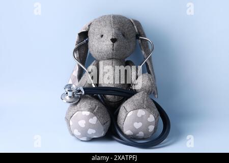 Lapin jouet avec stéthoscope sur fond bleu clair Banque D'Images