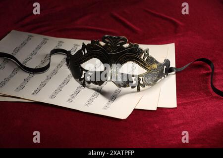 Masque facial élégant et feuilles de musique sur tissu rouge. Représentation théâtrale Banque D'Images