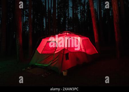 Une tente est éclairée de l'intérieur dans un terrain de camping forestier Banque D'Images