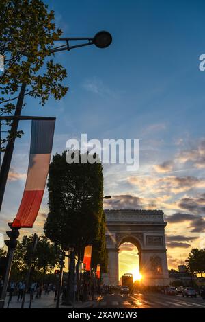 Magnifique coucher de soleil derrière l'Arc de Triomphe sur les champs-Élysées, avec drapeaux français affichés le long de l'avenue - Paris, France Banque D'Images