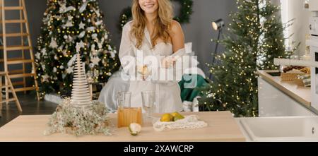 Femme cuisine décor de Noël en chemise blanche, peler des mandarines. Illustrer les préparatifs des fêtes du nouvel an. Banque D'Images