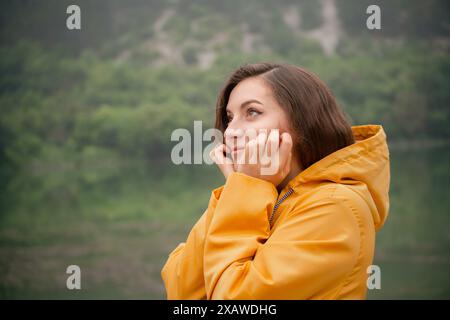 Une femme dans un imperméable jaune regarde au-dessus d'un plan d'eau. Elle est perdue dans la pensée, contemplant peut-être la beauté de la nature ou son propre pensionnat Banque D'Images