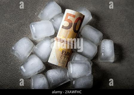 Concept de gel des fonds. Au-dessus de la vue de l'euro rouleau d'argent à l'intérieur des glaçons sur fond gris de studio. Copier l'espace. Banque D'Images