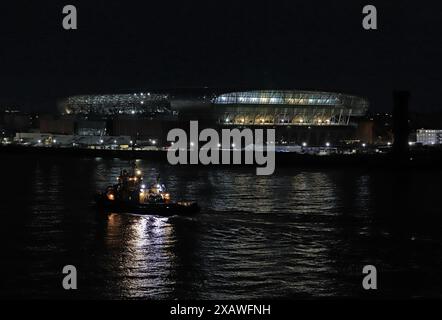 Dans l'obscurité, un remorqueur sur la rivière Mersey passe devant le nouveau terrain de football en cours de construction au quai Bramley Moore pour Everton FC Banque D'Images