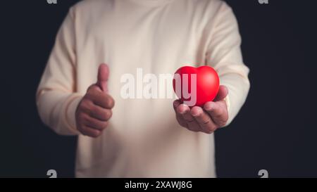 Homme tenant le jouet en forme de coeur et tout en se tenant debout sur fond gris, coeur dans la main gauche, Cardiologie, planification de la santé, assurance soins de santé et Medi Banque D'Images