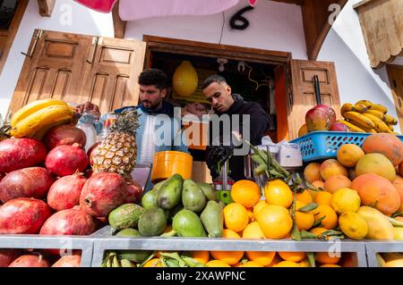 Deux hommes préparent des jus de fruits naturels dans leur commerce de jus frais de rue. Le magasin est très coloré et accueillant. Banque D'Images