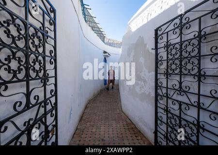 Un serveur apporte un plateau avec du thé marocain typique à travers une étroite ruelle blanche et des portes ouvertes en fer forgé à Rabat, la capitale du Maroc dans le nord de l'AF Banque D'Images