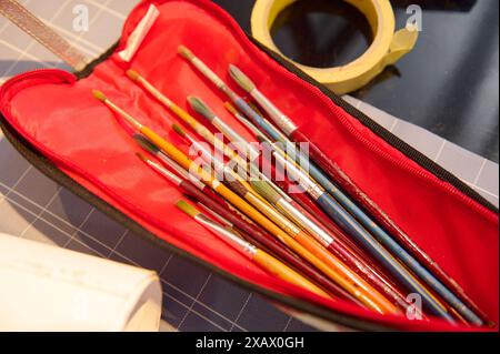 Pinceaux assortis soigneusement disposés dans un étui rouge placé sur une table de travail, prêts à être utilisés dans un atelier d'art ou une classe. Parfait pour les artistes, les étudiants, Banque D'Images