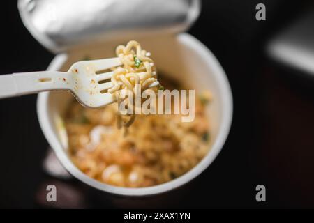 Une tasse de nouilles instantanées avec une fourchette en plastique. Les nouilles sont dans un bouillon avec des morceaux de viande et des légumes. Banque D'Images