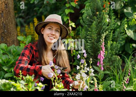 jeune femme jardinière taillant les fleurs avec sécateur dans le jardin Banque D'Images