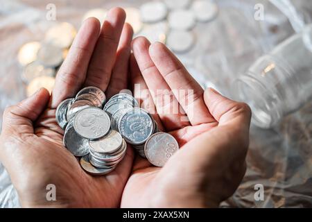 Une personne tenant une poignée de pièces d'argent avec les deux mains. Un pot avec plus de pièces de monnaie est visible en arrière-plan. Banque D'Images