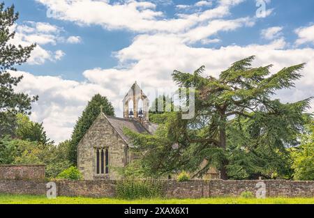 L'église de campagne de Saint Everilda à Poppleton près de York vue de l'autre côté d'un champ. Un mur de briques est au premier plan et un arbre est juste derrière Banque D'Images