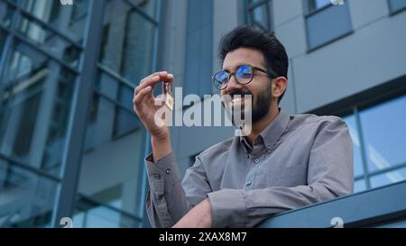 Homme souriant homme d'affaires indien arabe agent immobilier investisseur d'affaires tenir un tas de clés nouvel immeuble de bureaux de location d'appartement de ville à l'extérieur homme Banque D'Images