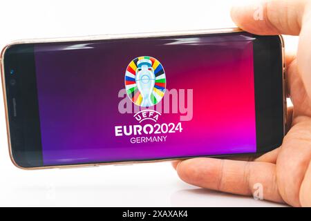 Un homme tient un smartphone avec le logo officiel du Championnat d'Europe de football de l'UEFA 2024 sur l'écran de son téléphone portable Banque D'Images
