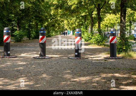 Une rangée de quatre poteaux rouges et blancs avec des sommets noirs se trouve dans un parc. Les poteaux sont placés dans une rangée, le premier sur la gauche et le dernier sur le Banque D'Images