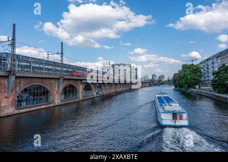 Un train rouge traverse un pont de briques rouges, et un bateau de passagers flotte le long de la rivière le long du pont. Divers modes de transport urbains. Banque D'Images