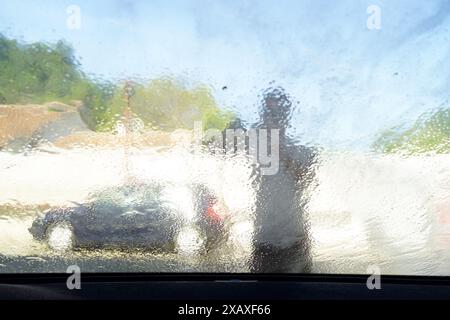 Lavage de la vitre avant avec un pistolet de lavage - un jet d'eau coulant d'un pistolet de lavage à haute pression, vue de l'intérieur de la voiture. Banque D'Images