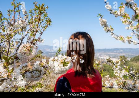 Femme en manteau rouge vue de derrière regardant le paysage de fleurs de cerisier. Fundão, Castelo Branco, Portugal Banque D'Images