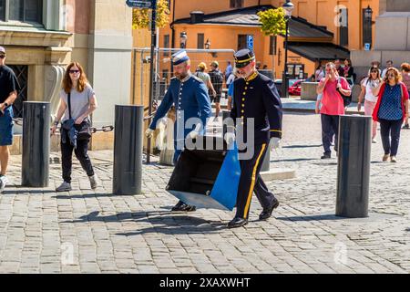Deux membres de la fanfare du changement de garde transportent un pupitre de musique noir pliant à travers la place pavée devant Kungliga Slottet, le palais royal de Stockholm. Le changement de garde y a lieu avec l'accompagnement musical de la fanfare montée. Stockholm, comté de Stockholm, Suède. Banque D'Images