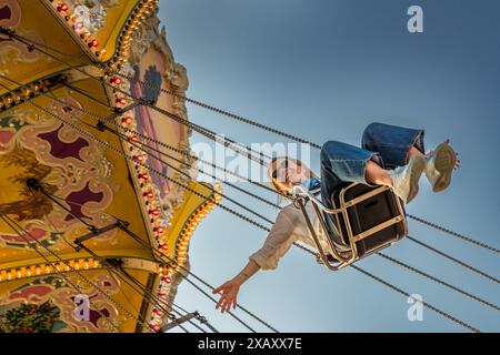 Détail avec les passagers sur le carrousel de chaîne nostalgique dans le soleil du soir. Gröna Lund sur l'île aux musées de Djurgården est le plus ancien parc d'attractions de Suède. Elle a été fondée en 1883 par l'Allemand Jacob Schultheiss. Le parc d'attractions est divisé en une ancienne et une nouvelle partie. Carrousel à chaînes à Gröna Lund Tivoli. Parc d'attractions saisonnier avec montagnes russes et manèges à sensations fortes, jeux compétitifs et concerts. Djurgårdsstaden, Stockholm, Suède Banque D'Images