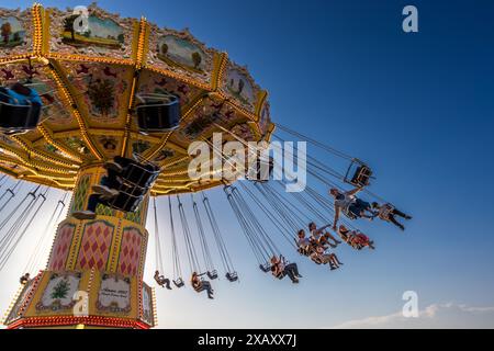 Détail avec les passagers sur le carrousel de chaîne nostalgique dans le soleil du soir. Le carrousel est situé directement sur l'eau. Carrousel à chaînes à Gröna Lund Tivoli. Parc d'attractions saisonnier avec montagnes russes et manèges à sensations fortes, jeux compétitifs et concerts. Djurgårdsstaden, Stockholm, Suède Banque D'Images