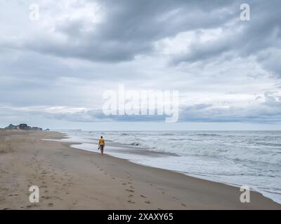 Femelle célibataire pieds nus marchant le long du rivage de l'océan Atlantique vers Rodanthe Pier sur Cape Hatteras en Caroline du Nord, États-Unis Banque D'Images