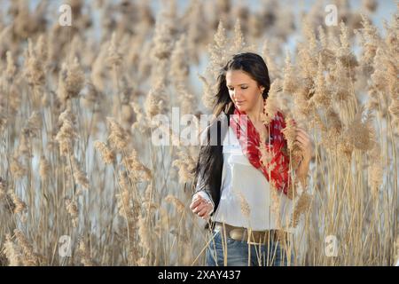 Femme brune portant une écharpe rouge et une chemise blanche marchant à travers de grandes herbes sèches, Bavière Banque D'Images