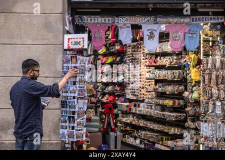 Barcelone, Espagne. 09 juin 2024. Le commis d'une boutique de souvenirs touristiques est vu réapprovisionner des cartes postales pour la vente. Comme la plupart des capitales européennes, Barcelone vit entre la nécessité d'une économie touristique dont elle ne peut se passer et le rejet d'un grand nombre de citoyens contre la distorsion culturelle et la précarité de l'emploi typiques de l'industrie touristique. Les slogans sur les espaces publics de la dernière manifestation contre la surpopulation touristique coexistent avec une activité touristique qui ne se repose jamais. Crédit : SOPA images Limited/Alamy Live News Banque D'Images