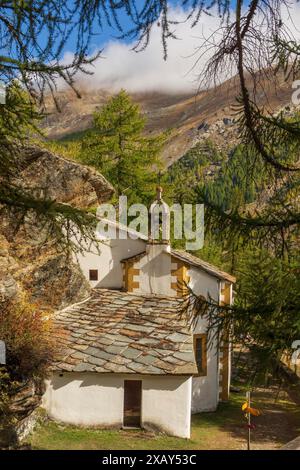 Petite église avec clocher, entourée de forêt et de montagnes dans un paysage alpin automnal, Saas Fee, Suisse Banque D'Images