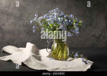 Bouquet de belles fleurs oublie-me-pas dans une cruche en verre et un tissu sur une table grise Banque D'Images