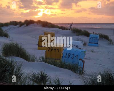 Coucher de soleil sur la plage avec des chaises de plage colorées devant les dunes et la mer, le ciel est illuminé de couleurs chaudes, juist, frise orientale, allemagne Banque D'Images