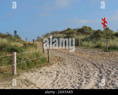 Sentier sablonneux mène à travers les dunes et la végétation, un signe de croix rouge est visible sous un ciel bleu, juist, frise orientale, allemagne Banque D'Images