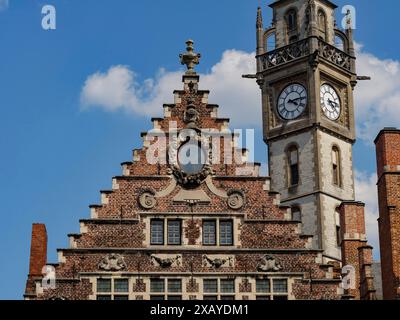 Une tour de l'horloge frappante et le pignon d'une maison en briques se détachent sur un ciel bleu, Gand, Belgique Banque D'Images