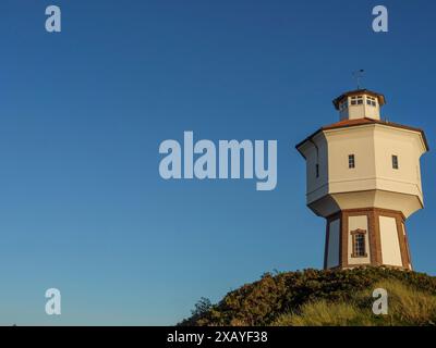 Un phare blanc avec un toit rouge sur une colline sous un ciel clair plus tard dans la journée, langeoog, allemagne Banque D'Images