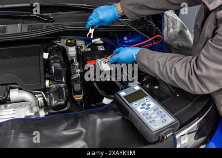 Maître mécanicien de voiture vérifiant et testant la batterie automobile avec testeur de batterie électronique numérique et analyseur dans l'atelier de véhicule automobile. Banque D'Images