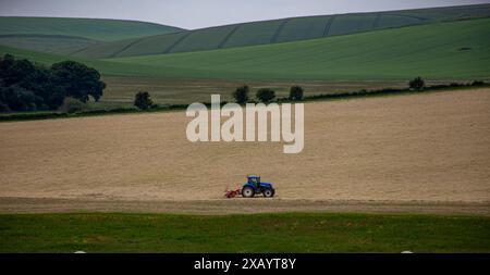 Tracteur cultivant des terres avec des collines verdoyantes en arrière-plan sous un ciel nuageux Banque D'Images