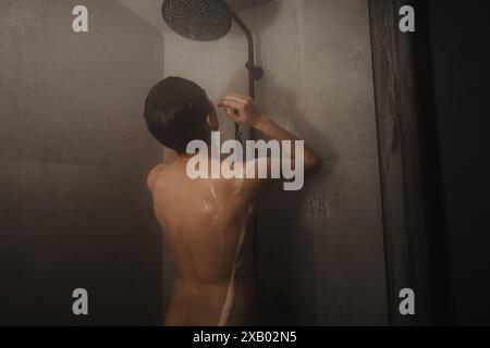 Homme prenant une douche, ajustant la température de l'eau dans une salle de bain moderne Banque D'Images