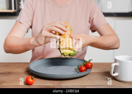 femme faisant sandwich avec baguette et fromage, le tenant dans les mains et se préparant à mordre, faisant le petit déjeuner, thème de routage du matin Banque D'Images