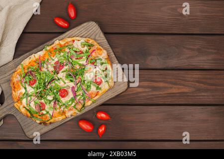 Une pizza napolitaine fraîchement cuite garnie de légumes et d'anchois sur une planche de bois, vue de dessus Banque D'Images