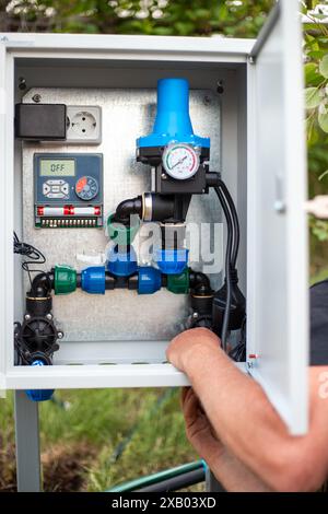 Assemblage d'un système automatique d'alimentation en eau pour l'irrigation goutte à goutte. Un homme installe une boîte d'assemblage. Banque D'Images