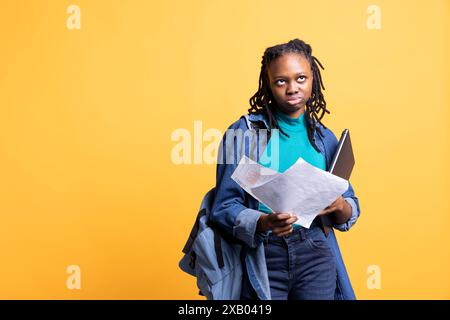 Femme afro-américaine roulant les yeux, travail de comptabilité, regarder les pages de rapport, se sentir ennuyé, fond de studio. Jeune fille frustrée après avoir lu des documents toute la journée tout en résolvant des tâches Banque D'Images