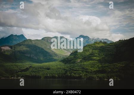 Un paysage à couper le souffle de collines verdoyantes et de montagnes imposantes sous un ciel partiellement nuageux en Alaska, mettant en valeur la beauté sereine et le sple naturel Banque D'Images