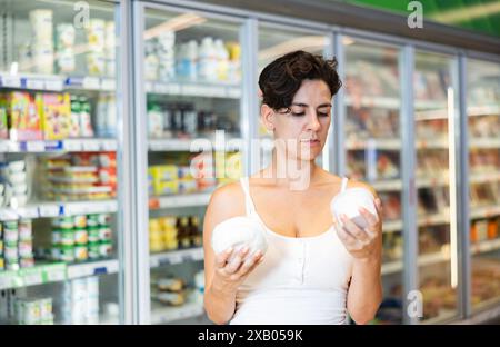 Une femme hispanique intéressée choisit des produits laitiers sur des étagères réfrigérées en magasin Banque D'Images