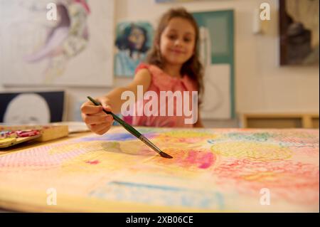 Fille appréciant la peinture dans un cours d'art. Jeune artiste créant des œuvres d'art vibrantes. Activité pédagogique créative et amusante pour les enfants. Banque D'Images